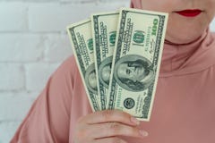 Молодая мусульманская женщина в розовых одеждах hijab держит денег наличных денег в банкнотах a доллара в ее руках стоковое фото rf Молодая мусульманская женщина в розовых одеждах hijab держит денег наличных денег в банкнотах a доллара в ее руках стоковое фото rf