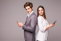 Молодая пара использует умные телефоны и усмехается пока стоящ спина к спине на серой предпосылке посмотрите камеру стоковые фотографии rf Молодая пара использует умные телефоны и усмехается пока стоящ спина к спине на серой предпосылке посмотрите камеру стоковые фотографии rf