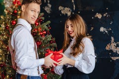 Молодая привлекательная девушка получает присутствующее от человека на предпосылке рождественской елки, концепции Нового Года стоковое изображение Молодая привлекательная девушка получает присутствующее от человека на предпосылке рождественской елки, концепции Нового Года стоковое изображение