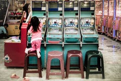 Молодое playfulgirl взбирается поверх стула пробуя достигнуть верхнюю часть машины аркады pinball стоковые изображения Молодое playfulgirl взбирается поверх стула пробуя достигнуть верхнюю часть машины аркады pinball стоковые изображения