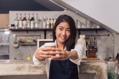 Молодое азиатское женское владение barista чашка кофе служа к ее клиенту с улыбкой окруженному с предпосылкой счетчика бара стоковые изображения rf Молодое азиатское женское владение barista чашка кофе служа к ее клиенту с улыбкой окруженному с предпосылкой счетчика бара стоковые изображения rf