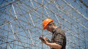 Молодой архитектор держа таблетку и смотря установку металла на предпосылку, планируя и конструируя новый проект сток-видео Молодой архитектор держа таблетку и смотря установку металла на предпосылку, планируя и конструируя новый проект сток-видео