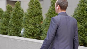 Молодой бизнесмен идя с беспроводными наушниками и счастливо связывает на телефонном звонке Молодой бизнесмен идя с беспроводными наушниками и счастливо связывает на телефонном звонке