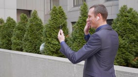 Молодой бизнесмен приходит с беспроводными наушниками в его ушах и сч Молодой бизнесмен приходит с беспроводными наушниками в его ушах и сч
