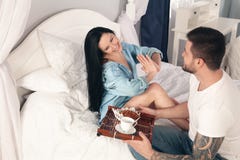 Молодой, красивый молодой человек принес круассаны и кофе на завтрак в кровати к его любимой девушке стоковая фотография Молодой, красивый молодой человек принес круассаны и кофе на завтрак в кровати к его любимой девушке стоковая фотография