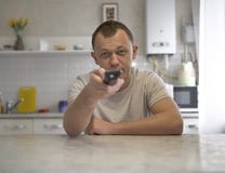 Молодой парень с каналами переключателей дистанционного управления ТВ пока сидящ в кухне, виде спереди стоковая фотография rf Молодой парень с каналами переключателей дистанционного управления ТВ пока сидящ в кухне, виде спереди стоковая фотография rf