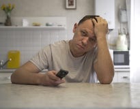 Молодой привлекательный парень с ТВ удаленным сидит в кухне стоковые фотографии rf Молодой привлекательный парень с ТВ удаленным сидит в кухне стоковые фотографии rf