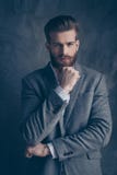 Молодой стильный бородатый парень с усиком в костюме стоит на gr стоковая фотография Молодой стильный бородатый парень с усиком в костюме стоит на gr стоковая фотография