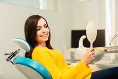 Молодой счастливый клиент женщины смотря зеркало с зубастой улыбкой на зубоврачебном офисе стоковое изображение Молодой счастливый клиент женщины смотря зеркало с зубастой улыбкой на зубоврачебном офисе стоковое изображение