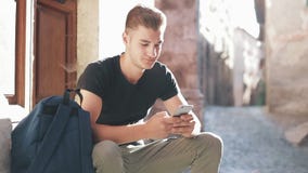 Молодой турист при рюкзак сидя на лестницах входа и используя мобильный телефон сток-видео Молодой турист при рюкзак сидя на лестницах входа и используя мобильный телефон сток-видео
