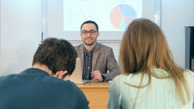Молодой учитель сидя в классе школы при компьтер-книжка, говоря к студентам стоковые изображения rf Молодой учитель сидя в классе школы при компьтер-книжка, говоря к студентам стоковые изображения rf
