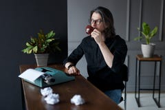 Молодой человек в черных стеклах рубашки и глаза, выпивает кофе на работая столе для идеи работы, над серыми интерьерами стоковое фото Молодой человек в черных стеклах рубашки и глаза, выпивает кофе на работая столе для идеи работы, над серыми интерьерами стоковое фото