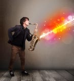 Молодой человек играя на саксофоне с цветастыми звуковыми войнами Стоковое Изображение Молодой человек играя на саксофоне с цветастыми звуковыми войнами Стоковое Изображение