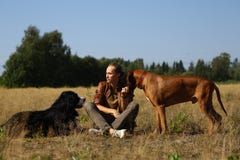 Молодой человек идя с собакой горы Bernese 2 собак и ridgeback на поле лета стоковые фотографии rf Молодой человек идя с собакой горы Bernese 2 собак и ridgeback на поле лета стоковые фотографии rf