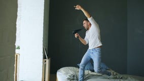 Молодой человек поя к фену для волос и танцуя rocknroll на кровати в спальне стоковая фотография Молодой человек поя к фену для волос и танцуя rocknroll на кровати в спальне стоковая фотография