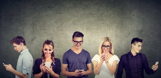 Молодые вскользь люди используя мобильный телефон стоя совместно против бетонной стены стоковое изображение rf Молодые вскользь люди используя мобильный телефон стоя совместно против бетонной стены стоковое изображение rf