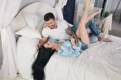 Молодые пары лежа в кровати и смеясь над пока щекочущ один другого стоковое изображение rf Молодые пары лежа в кровати и смеясь над пока щекочущ один другого стоковое изображение rf