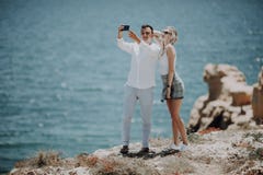 Молодые пары принимая фото автопортрета selfie на верхней части скалы на предпосылке океана Счастливые любовники, женщина и челов стоковое изображение Молодые пары принимая фото автопортрета selfie на верхней части скалы на предпосылке океана Счастливые любовники, женщина и челов стоковое изображение
