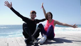 Молодые привлекательные счастливые пары поднимая руки вверх в усаживании воздуха усмехаясь и веселя на пляже ( сток-видео Молодые привлекательные счастливые пары поднимая руки вверх в усаживании воздуха усмехаясь и веселя на пляже ( сток-видео