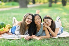 3 молодых счастливых multiracial женщины лежа на траве в парке стоковая фотография rf 3 молодых счастливых multiracial женщины лежа на траве в парке стоковая фотография rf