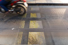 Мотоцикл обеспечивая циркуляцию на мосте с полом решетки металла стоковые фотографии rf Мотоцикл обеспечивая циркуляцию на мосте с полом решетки металла стоковые фотографии rf