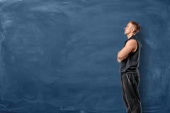 Мышечный молодой человек стоит его пересеченные оружия и смотрит вверх на голубой предпосылке доски стоковое фото rf Мышечный молодой человек стоит его пересеченные оружия и смотрит вверх на голубой предпосылке доски стоковое фото rf