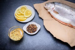 На темном - серая столешница лежит полинянная рыба на бумаге kraft плита с солью перца лимона и специями и маслом стоковые изображения rf На темном - серая столешница лежит полинянная рыба на бумаге kraft плита с солью перца лимона и специями и маслом стоковые изображения rf