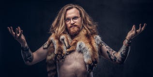 Нагой tattoed мужчина битника redhead при длинные luxuriant волосы и полная борода представляя с кожами лисы на его плечах внутри стоковое фото rf Нагой tattoed мужчина битника redhead при длинные luxuriant волосы и полная борода представляя с кожами лисы на его плечах внутри стоковое фото rf