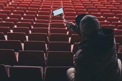 Насмешливый поднимающий вверх смартфон с ручкой selfie в руках человека на предпосылке стоек Парень принимает selfie на стоковые изображения rf Насмешливый поднимающий вверх смартфон с ручкой selfie в руках человека на предпосылке стоек Парень принимает selfie на стоковые изображения rf