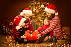 Настоящий момент отверстия семьи рождества, дерево и подарки Xmas, счастливый ребенок матери отца и младенец в красной шляпе стоковое изображение rf Настоящий момент отверстия семьи рождества, дерево и подарки Xmas, счастливый ребенок матери отца и младенец в красной шляпе стоковое изображение rf