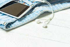 Наушники и смартфон в джинсах кармана старых в винтажном стиле на белой деревянной предпосылке с copyspace стоковые изображения rf Наушники и смартфон в джинсах кармана старых в винтажном стиле на белой деревянной предпосылке с copyspace стоковые изображения rf