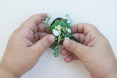 Небольшая зеленая лягушка сделанная из стекла в руках ребенка на белой предпосылке стоковое изображение Небольшая зеленая лягушка сделанная из стекла в руках ребенка на белой предпосылке стоковое изображение