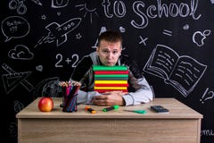 Несчастная малолетка сидя на столе при куча книг под подбородком, окруженная с школьными принадлежностями chalkboard стоковые изображения Несчастная малолетка сидя на столе при куча книг под подбородком, окруженная с школьными принадлежностями chalkboard стоковые изображения