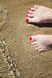 Ноги женщины pedicured с красным маникюром на пальцах ноги в песке в воде стоковое фото Ноги женщины pedicured с красным маникюром на пальцах ноги в песке в воде стоковое фото