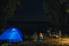 Ночь располагаясь лагерем на береге озера Человек и женщина сидят Соедините туристов наслаждаясь изумляющ взгляд ночного неба пол стоковая фотография Ночь располагаясь лагерем на береге озера Человек и женщина сидят Соедините туристов наслаждаясь изумляющ взгляд ночного неба пол стоковая фотография