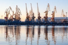 Одесса, Украина - Januadry 02, 2017: Краны в терминале порта груза, краны контейнера груза отразили в воде Заход солнца стоковое фото rf Одесса, Украина - Januadry 02, 2017: Краны в терминале порта груза, краны контейнера груза отразили в воде Заход солнца стоковое фото rf