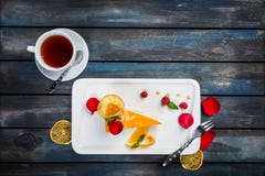 Оранжевый торт с полениками чашки чаю свежими на белой плите с лепестками розы Взгляд сверху Красивая деревянная предпосылка стоковые фотографии rf Оранжевый торт с полениками чашки чаю свежими на белой плите с лепестками розы Взгляд сверху Красивая деревянная предпосылка стоковые фотографии rf