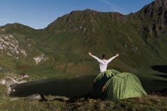 Оружия молодого человека подняли перед зеленым шатром в горах Швейцарии пока он наслаждается панорамным видом стоковое фото Оружия молодого человека подняли перед зеленым шатром в горах Швейцарии пока он наслаждается панорамным видом стоковое фото