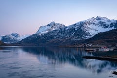 Остров Lofoten вечером, со снежными пиками в задней части и рыбацком поселке со светами города во фронте стоковые изображения Остров Lofoten вечером, со снежными пиками в задней части и рыбацком поселке со светами города во фронте стоковые изображения