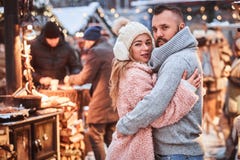 Очаровательная пара в любов, обнимая совместно и смотря камеру пока стоящ на ярмарке рождества стоковое фото rf Очаровательная пара в любов, обнимая совместно и смотря камеру пока стоящ на ярмарке рождества стоковое фото rf