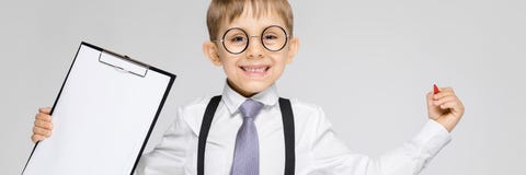 Очаровательный мальчик в белой рубашке, подтяжках, связи и джинсах света стоит на серой предпосылке Мальчик держит ручку и стоковые фотографии rf Очаровательный мальчик в белой рубашке, подтяжках, связи и джинсах света стоит на серой предпосылке Мальчик держит ручку и стоковые фотографии rf