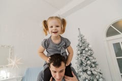 Очень красивая девушка сидит на плечах и игре ее папы, делая стороны в комнате Нового Года стоковая фотография rf Очень красивая девушка сидит на плечах и игре ее папы, делая стороны в комнате Нового Года стоковая фотография rf
