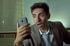 Очень удивленный человек смотря его смартфон в комнате стоковое изображение rf Очень удивленный человек смотря его смартфон в комнате стоковое изображение rf
