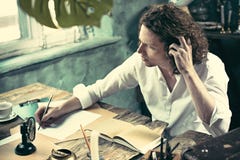 Писатель на работе Красивый молодой писатель сидя на таблице и писать что-то в его sketchpad стоковые фото Писатель на работе Красивый молодой писатель сидя на таблице и писать что-то в его sketchpad стоковые фото