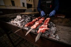 Повара рук в голубых перчатках держат протыкальники с мясом на гриле стоковое фото rf Повара рук в голубых перчатках держат протыкальники с мясом на гриле стоковое фото rf