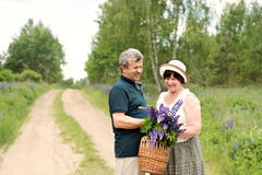 Пожилая пара идет через лес и человек дает женщине сплетенную корзину с букетом цветков фиолетовых lupines стоковые фото Пожилая пара идет через лес и человек дает женщине сплетенную корзину с букетом цветков фиолетовых lupines стоковые фото