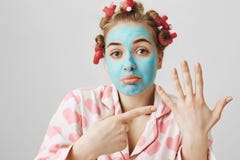 Портрет домохозяйки осадки смешной в pyjamas волос-curlers и голубом лицевом щитке гермошлема указывая на левую руку, спрашивая г стоковая фотография rf Портрет домохозяйки осадки смешной в pyjamas волос-curlers и голубом лицевом щитке гермошлема указывая на левую руку, спрашивая г стоковая фотография rf