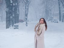 Портрет зимы женщины в белом пальто во время снежностей в парке Стоковые Изображения Портрет зимы женщины в белом пальто во время снежностей в парке Стоковые Изображения