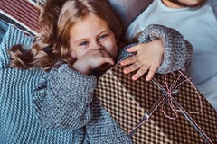 Портрет конца-вверх счастливой маленькой девочки в теплом свитере держит подарки пока лежащ на кровати стоковое фото rf Портрет конца-вверх счастливой маленькой девочки в теплом свитере держит подарки пока лежащ на кровати стоковое фото rf