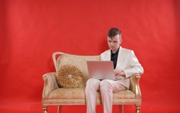 Портрет костюма и сидеть офиса человека подростка нося белого на золотой роскошной софе на красной предпосылке он работает на Ла стоковое фото Портрет костюма и сидеть офиса человека подростка нося белого на золотой роскошной софе на красной предпосылке он работает на Ла стоковое фото
